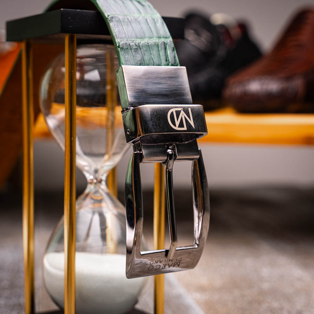 The Riccardo Belt Forest Green by Marco Di Milano features crocodile-embossed dark green leather and a silver buckle engraved with the brand logo, displayed coiled on a white background.