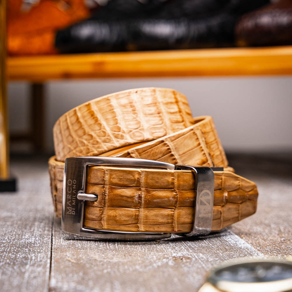 The Riccardo Belt Oil Orix by Marco Di Milano features genuine exotic leather with a crocodile pattern, a silver engraved buckle, and brand logos—elegantly coiled on a white background.
