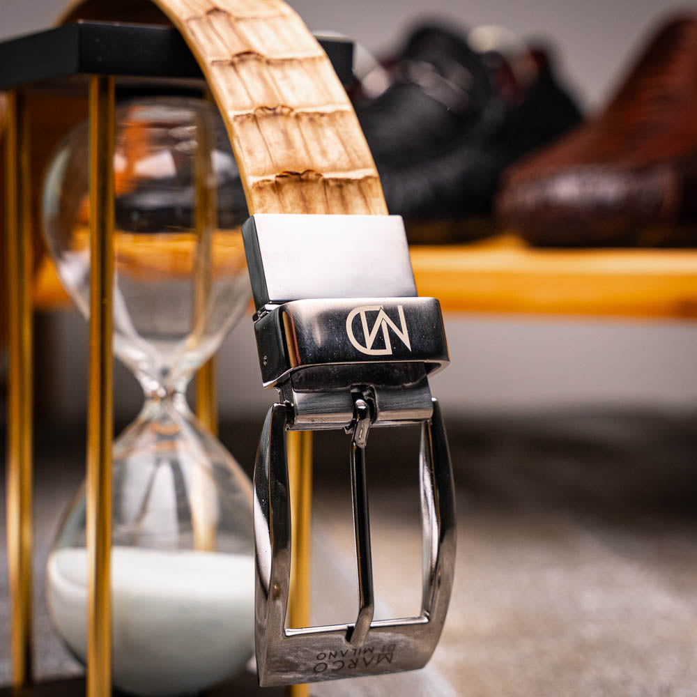 The Riccardo Belt Oil Orix by Marco Di Milano features genuine exotic leather with a crocodile pattern, a silver engraved buckle, and brand logos—elegantly coiled on a white background.