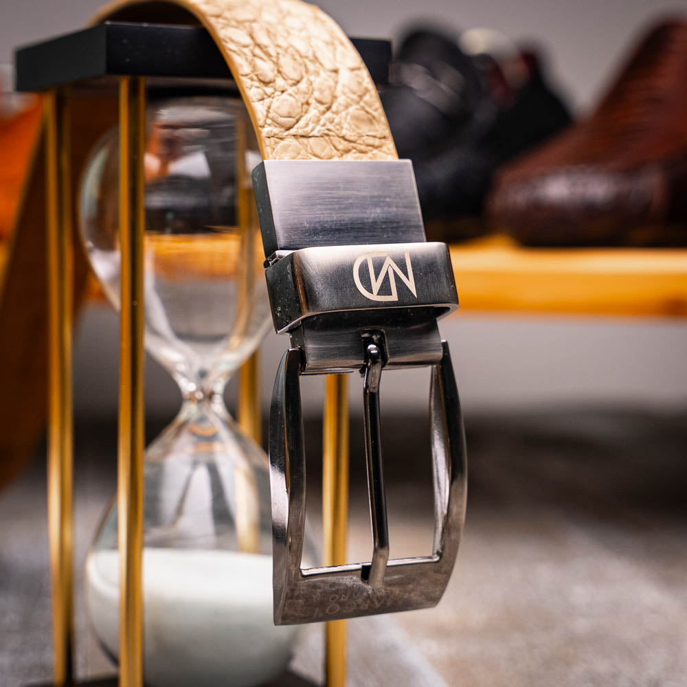 The Riccardo Belt Orix by Marco Di Milano is a rolled tan caiman fuscus-belly belt with an engraved silver buckle, shown on a white background—a genuine exotic accessory.