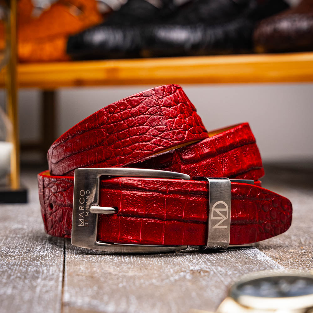 The Riccardo Belt Red by Marco Di Milano, crafted from genuine caiman fuscus-belly leather with a crocodile texture and a silver engraved buckle, is elegantly displayed coiled on a white background—perfect for refined style.