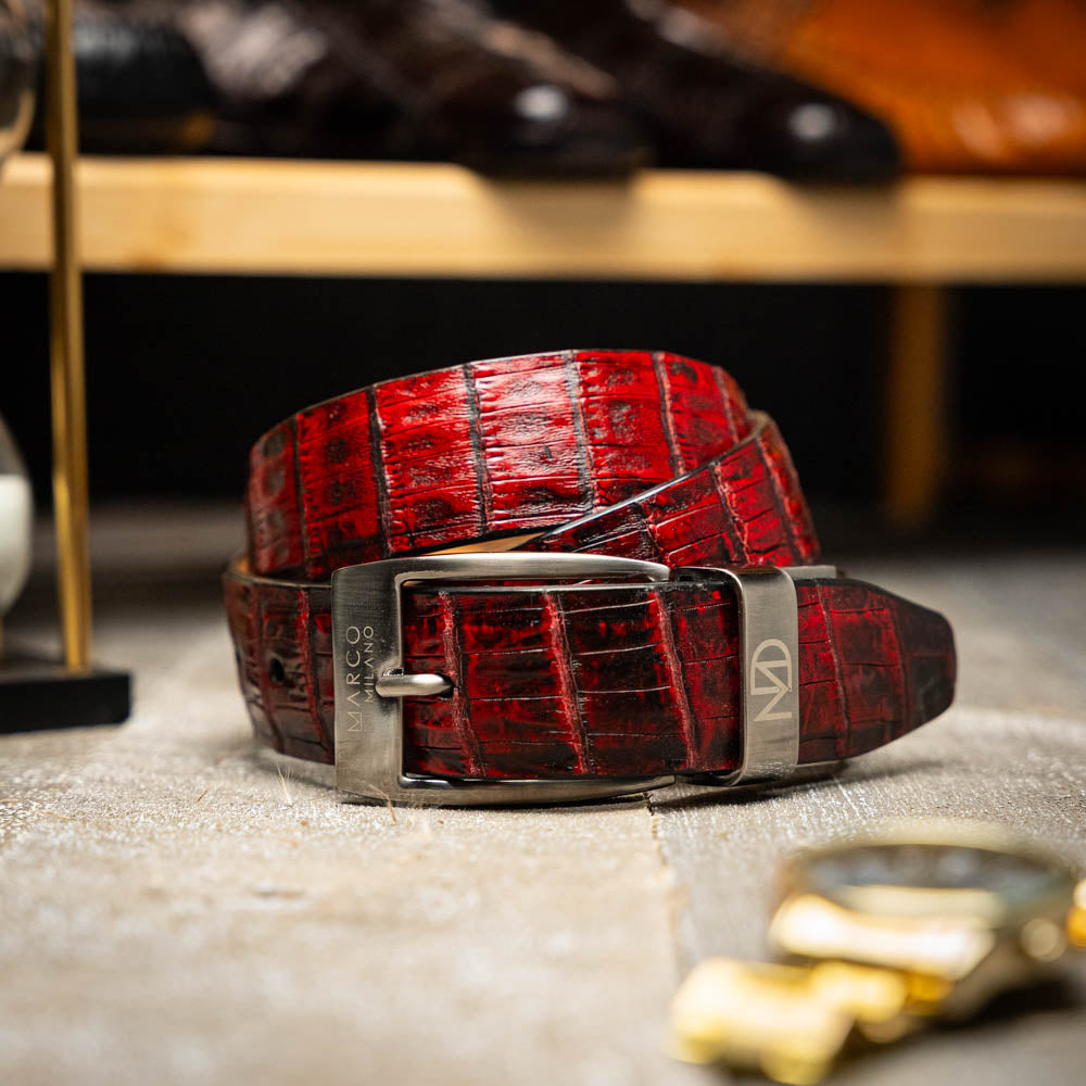The Riccardo Belt Black Cherry by Marco Di Milano is a genuine caiman fuscus-belly belt in red and black, featuring a silver buckle engraved with the brand’s logo—perfect for lovers of fine exotics.