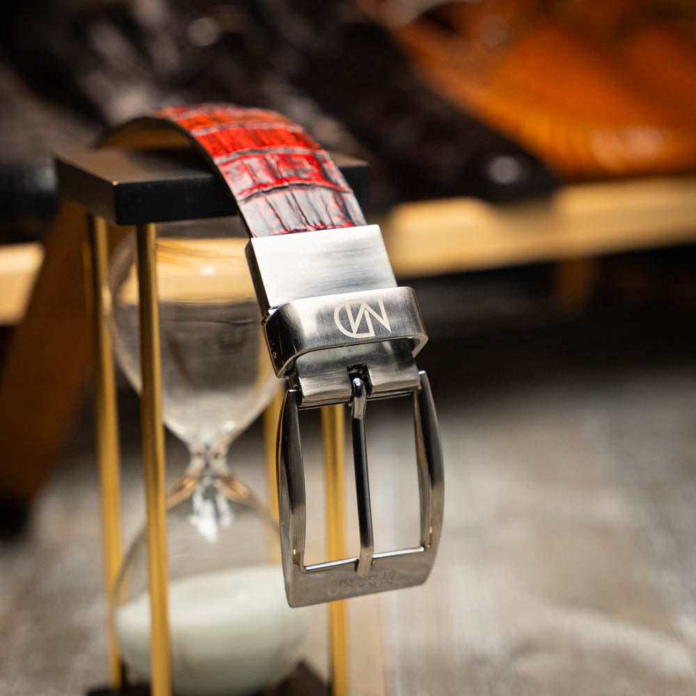 The Riccardo Belt Black Cherry by Marco Di Milano is a genuine caiman fuscus-belly belt in red and black, featuring a silver buckle engraved with the brand’s logo—perfect for lovers of fine exotics.