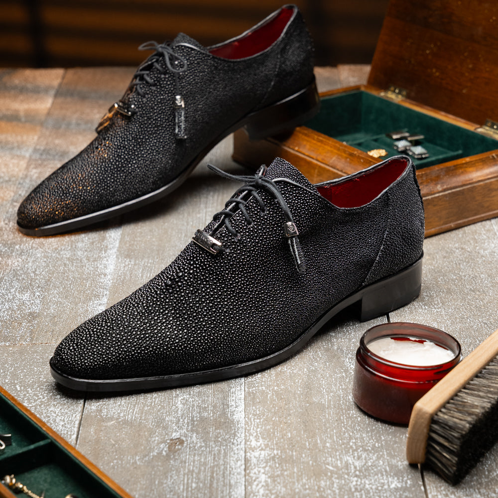 A pair of Rimini Black luxury dress shoes by Marco Di Milano, featuring a black textured finish and lace-up closure—one shoe displayed upright while the other shows the brown leather sole with embossed branding.