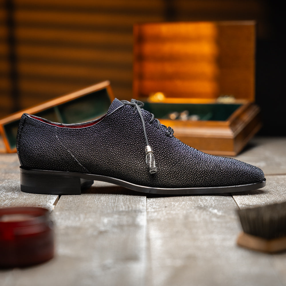 A pair of Rimini Black luxury dress shoes by Marco Di Milano, featuring a black textured finish and lace-up closure—one shoe displayed upright while the other shows the brown leather sole with embossed branding.