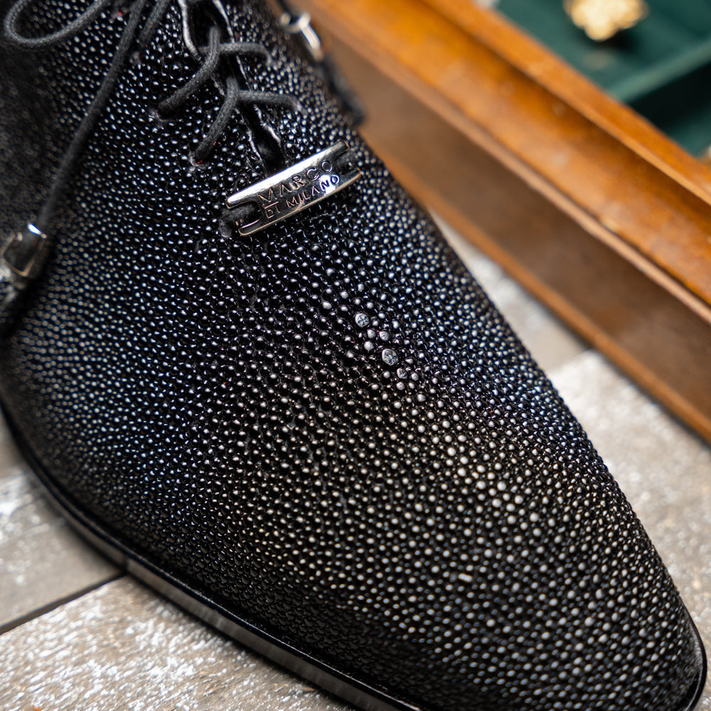 A pair of Rimini Black luxury dress shoes by Marco Di Milano, featuring a black textured finish and lace-up closure—one shoe displayed upright while the other shows the brown leather sole with embossed branding.