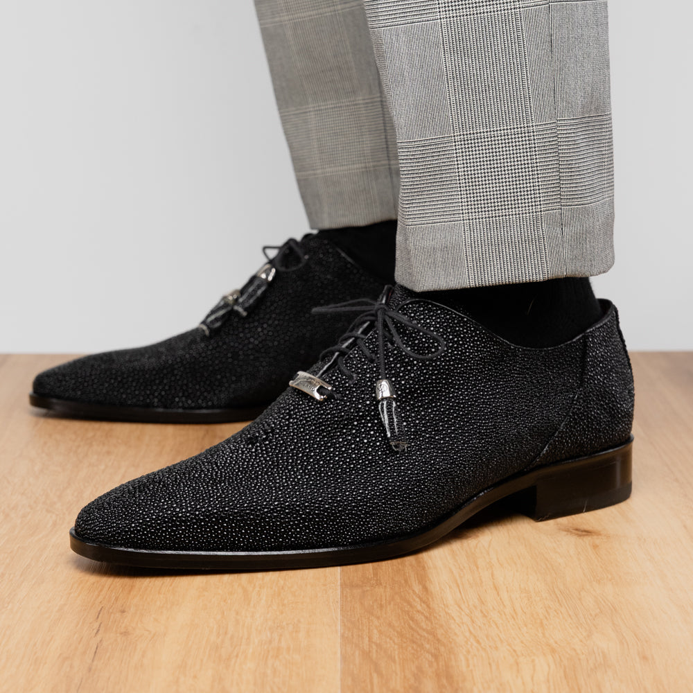 A pair of Rimini Black luxury dress shoes by Marco Di Milano, featuring a black textured finish and lace-up closure—one shoe displayed upright while the other shows the brown leather sole with embossed branding.