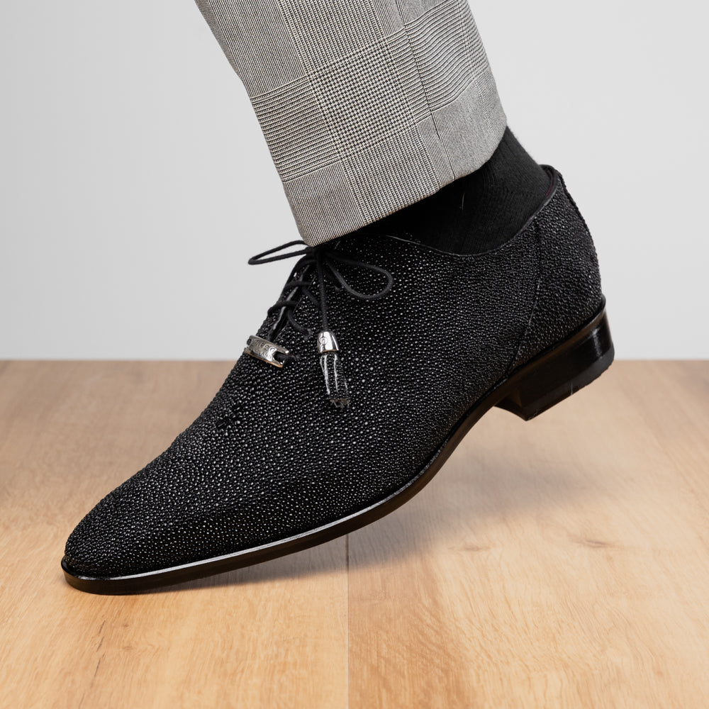 A pair of Rimini Black luxury dress shoes by Marco Di Milano, featuring a black textured finish and lace-up closure—one shoe displayed upright while the other shows the brown leather sole with embossed branding.