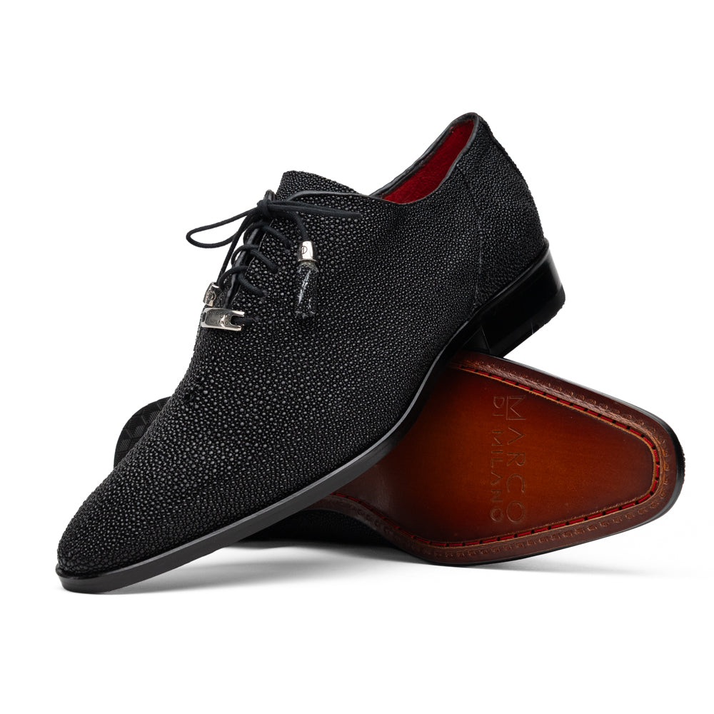 A pair of Rimini Black luxury dress shoes by Marco Di Milano, featuring a black textured finish and lace-up closure—one shoe displayed upright while the other shows the brown leather sole with embossed branding.