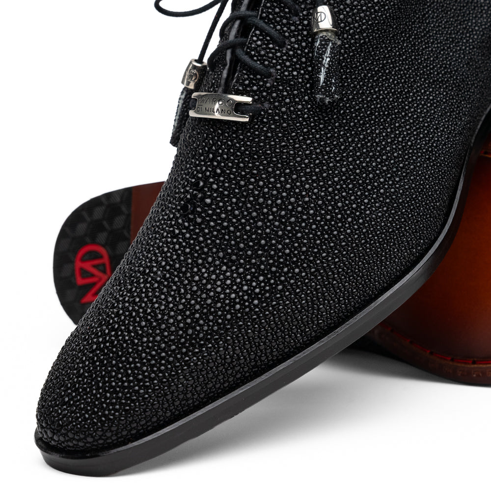 A pair of Rimini Black luxury dress shoes by Marco Di Milano, featuring a black textured finish and lace-up closure—one shoe displayed upright while the other shows the brown leather sole with embossed branding.