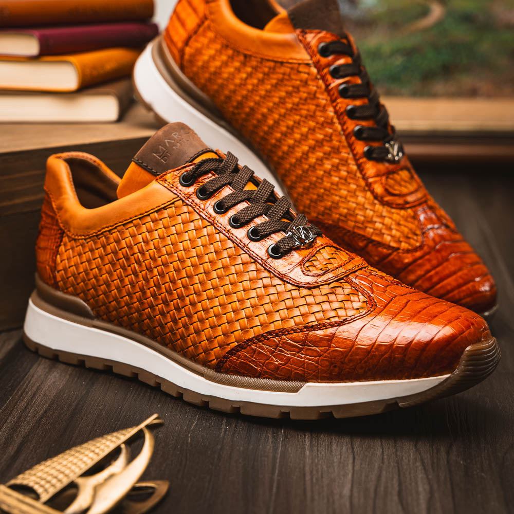 The Roma Brandy sneakers by Marco Di Milano feature brown woven calfskin, textured toe and heel, black laces, white midsoles, and brown rubber outsoles. One shoe stands upright while the other lies on its side.