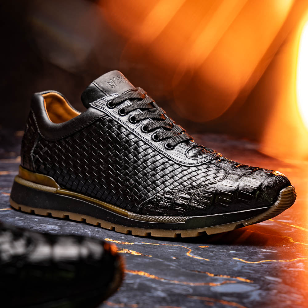The Marco Di Milano Roma Black features luxury black woven calfskin sneakers with black laces and brown rubber soles—one shoe stands upright while the other leans against it.