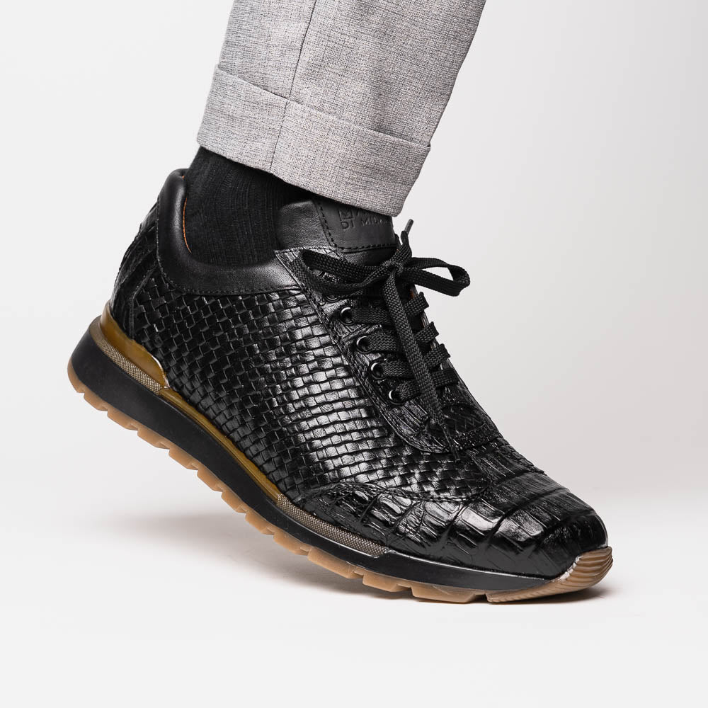 The Marco Di Milano Roma Black features luxury black woven calfskin sneakers with black laces and brown rubber soles—one shoe stands upright while the other leans against it.