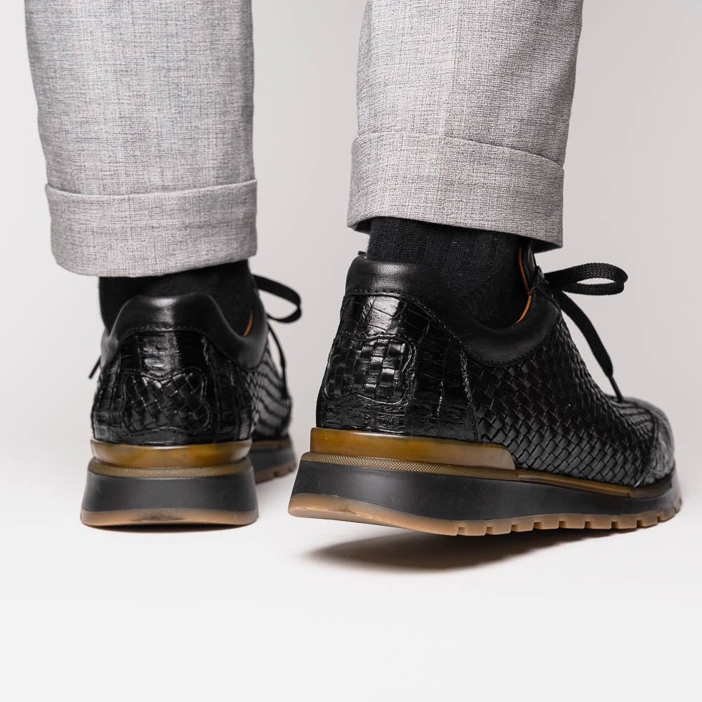 The Marco Di Milano Roma Black features luxury black woven calfskin sneakers with black laces and brown rubber soles—one shoe stands upright while the other leans against it.