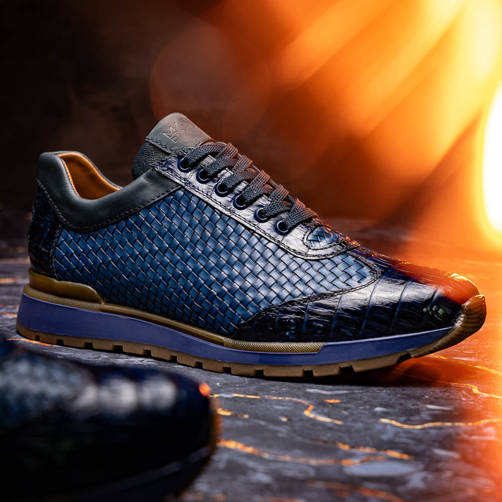 A pair of Marco Di Milano's Roma Navy sneakers: blue woven calfskin with brown rubber soles, one upright and the other leaning, highlighting the distinct tread pattern in elegant style.