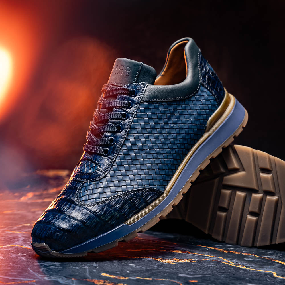 A pair of Marco Di Milano's Roma Navy sneakers: blue woven calfskin with brown rubber soles, one upright and the other leaning, highlighting the distinct tread pattern in elegant style.