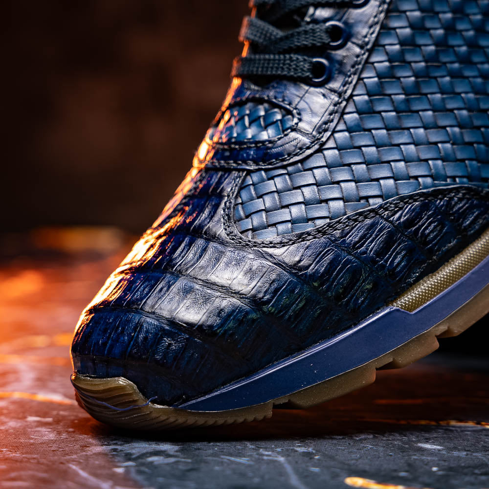 A pair of Marco Di Milano's Roma Navy sneakers: blue woven calfskin with brown rubber soles, one upright and the other leaning, highlighting the distinct tread pattern in elegant style.