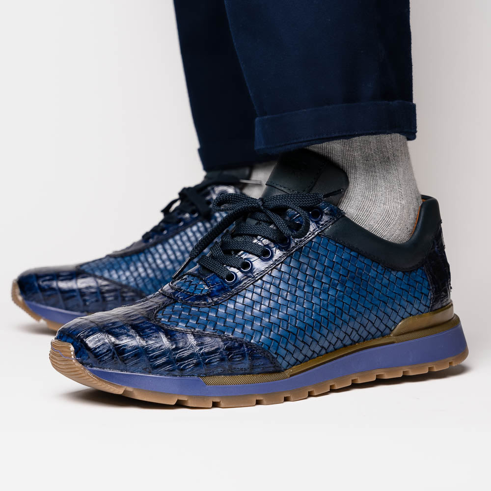 A pair of Marco Di Milano's Roma Navy sneakers: blue woven calfskin with brown rubber soles, one upright and the other leaning, highlighting the distinct tread pattern in elegant style.
