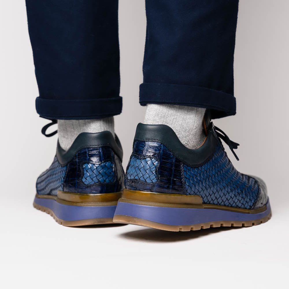 A pair of Marco Di Milano's Roma Navy sneakers: blue woven calfskin with brown rubber soles, one upright and the other leaning, highlighting the distinct tread pattern in elegant style.