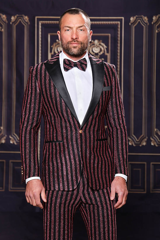A man wears the MANZINI HEATHER Men's Slim-Fit 2-Piece Glitter Stripe Stage Prom Suit in rose gold by Manzini, posing before an ornate dark backdrop.