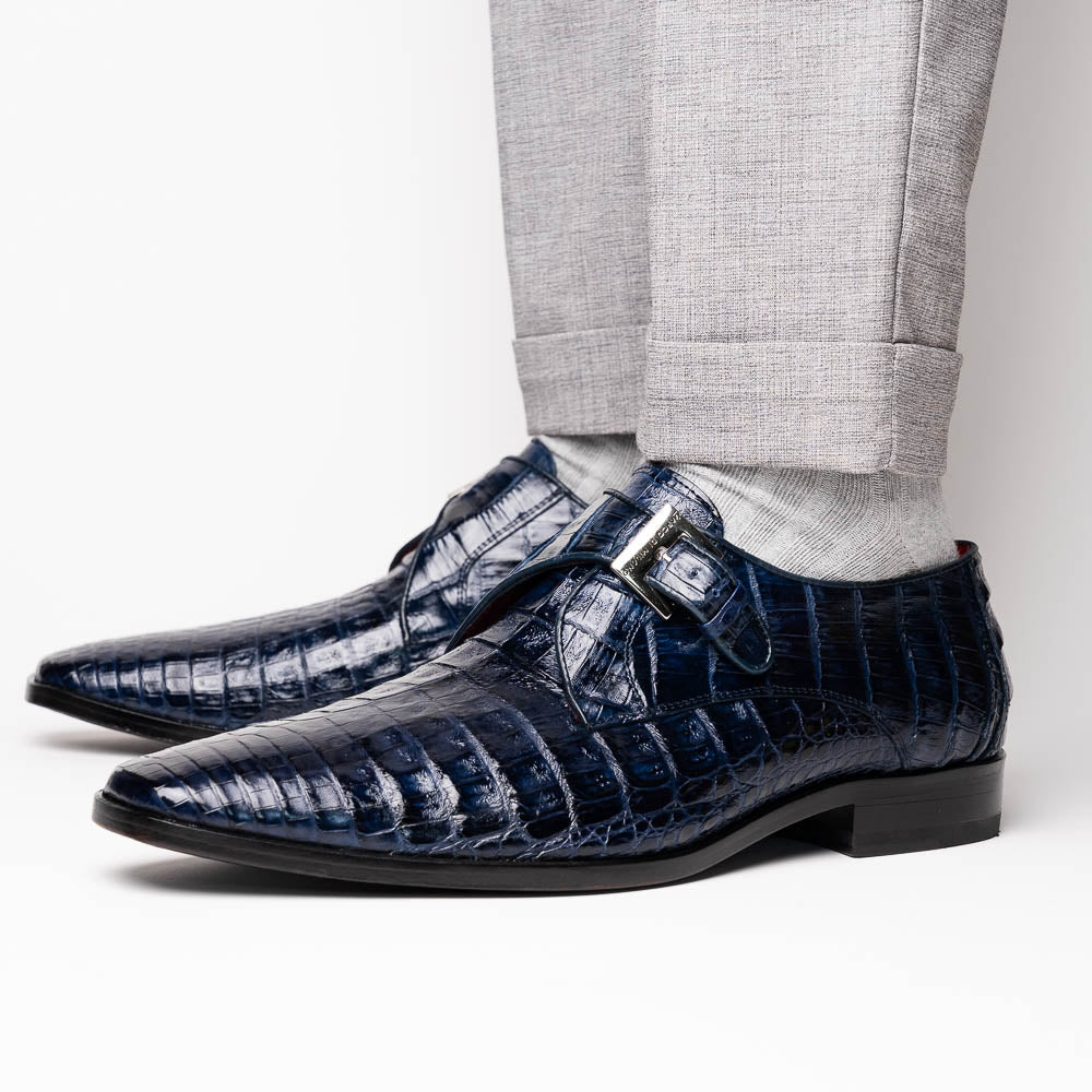 The Marco Di Milano Rovigo Navy features dark blue genuine caiman crocodile monk strap dress shoes with a silver buckle—one upright, the other on its side to display the sole—ideal for luxury men's footwear enthusiasts.