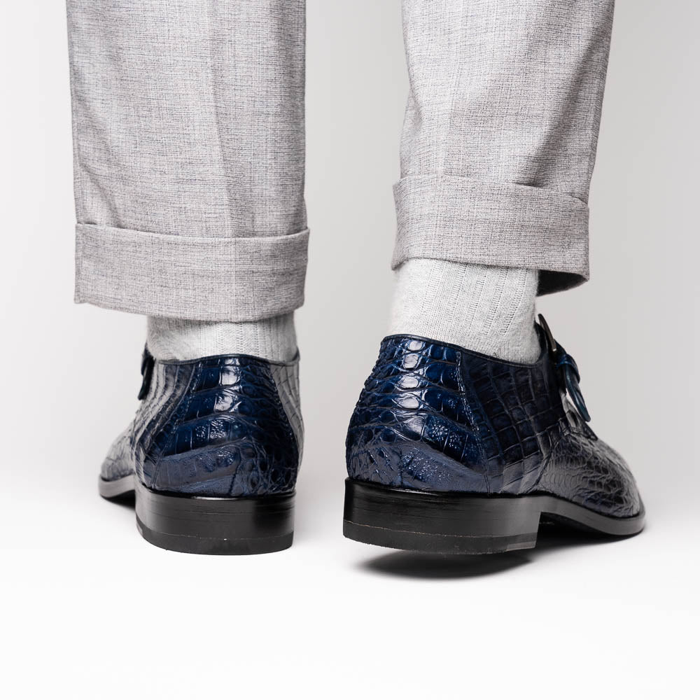 The Marco Di Milano Rovigo Navy features dark blue genuine caiman crocodile monk strap dress shoes with a silver buckle—one upright, the other on its side to display the sole—ideal for luxury men's footwear enthusiasts.
