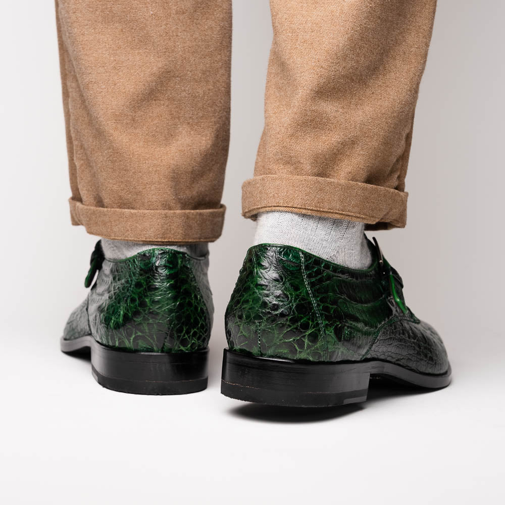 The Marco Di Milano Rovigo Forest Green features genuine caiman crocodile leather and a luxury monk strap, with one dress shoe propped to reveal its sole—a bold statement among men's exotic dress shoes.