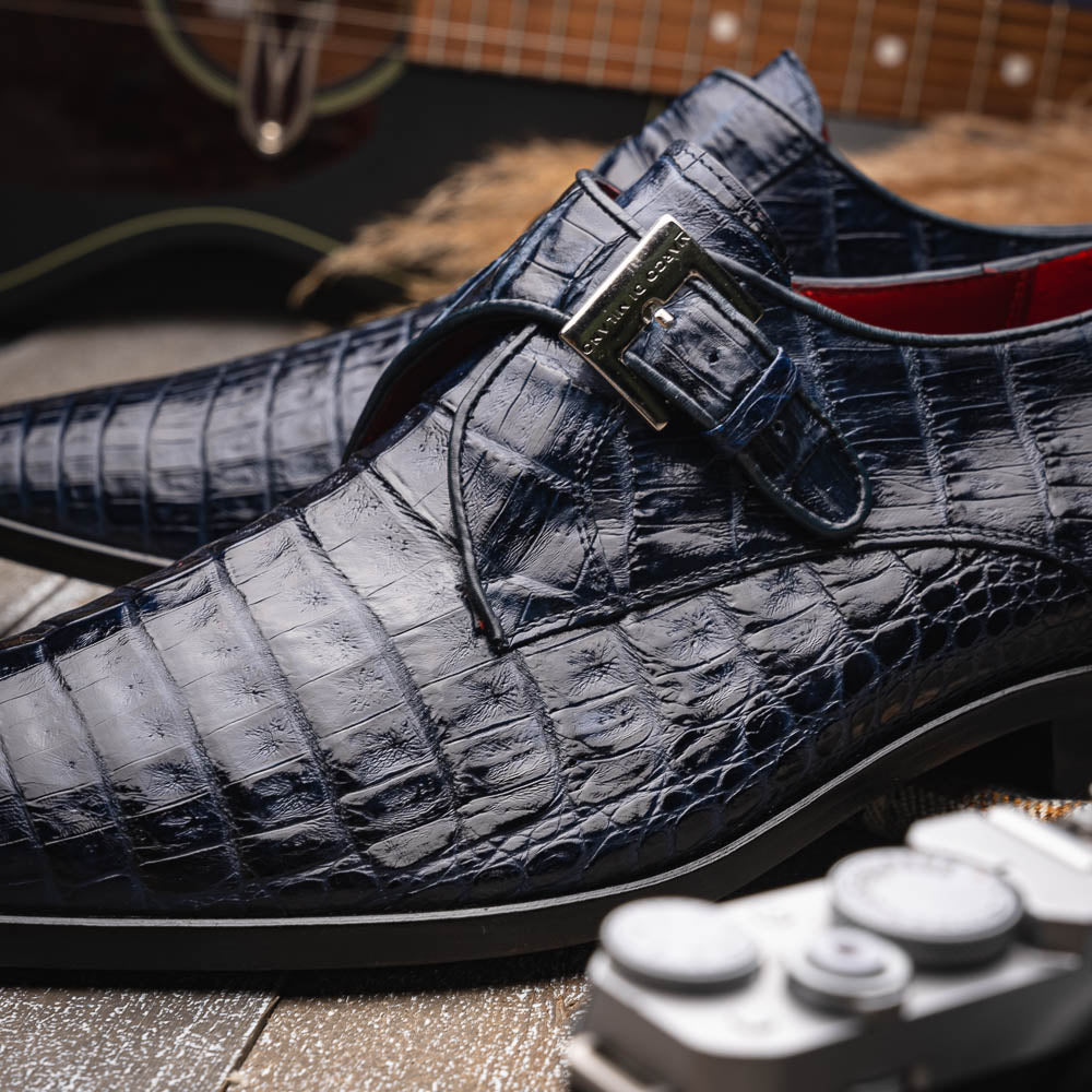 The Marco Di Milano Rovigo Navy features dark blue genuine caiman crocodile monk strap dress shoes with a silver buckle—one upright, the other on its side to display the sole—ideal for luxury men's footwear enthusiasts.