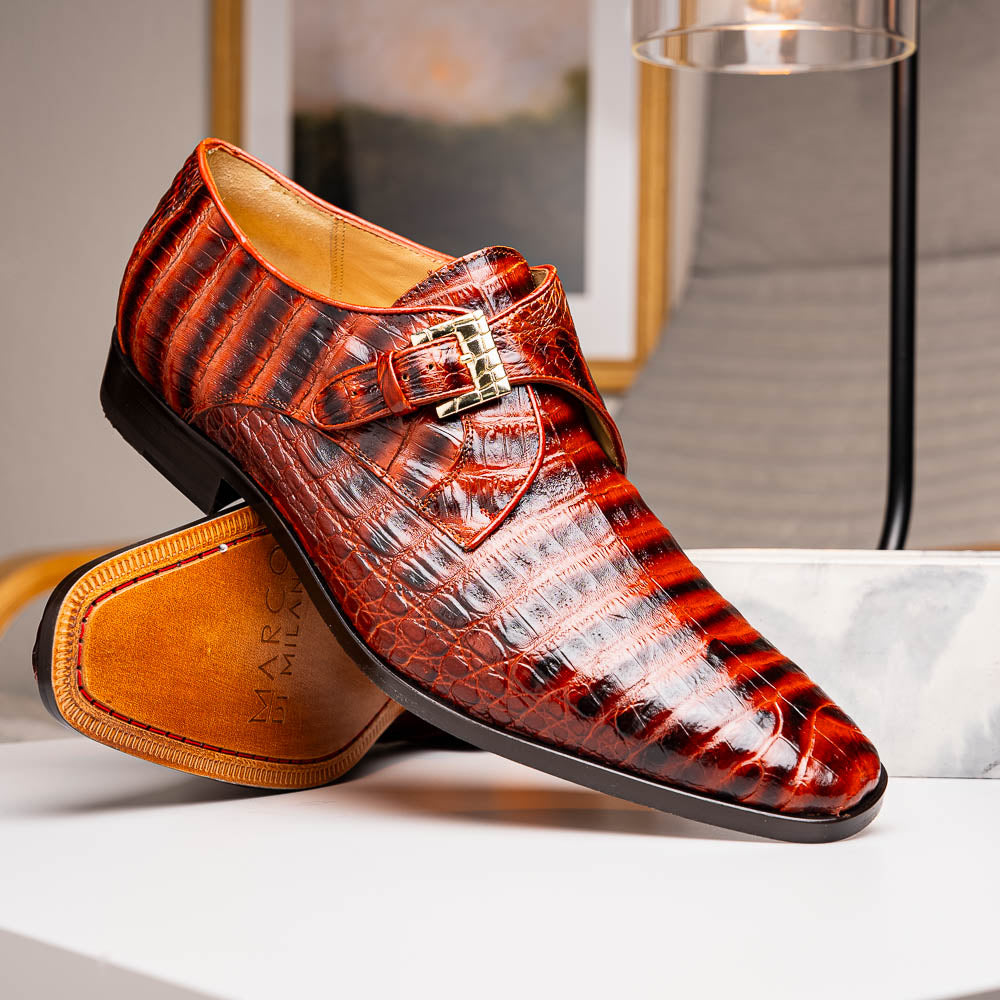 The Rovigo Cognac Straps by Marco Di Milano are brown genuine caiman crocodile monk strap dress shoes with a metal buckle—one upright, one on its side showing the branded sole. Luxury footwear for refined taste.