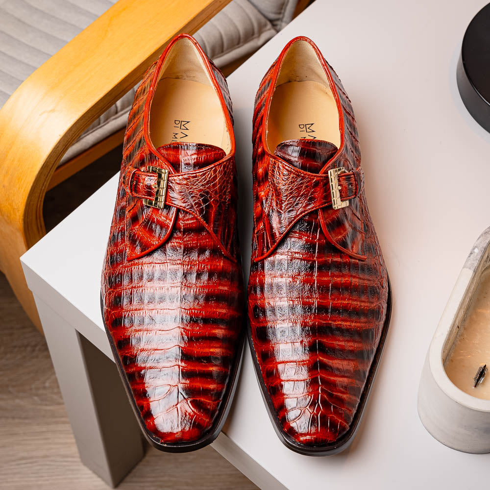 The Rovigo Cognac Straps by Marco Di Milano are brown genuine caiman crocodile monk strap dress shoes with a metal buckle—one upright, one on its side showing the branded sole. Luxury footwear for refined taste.