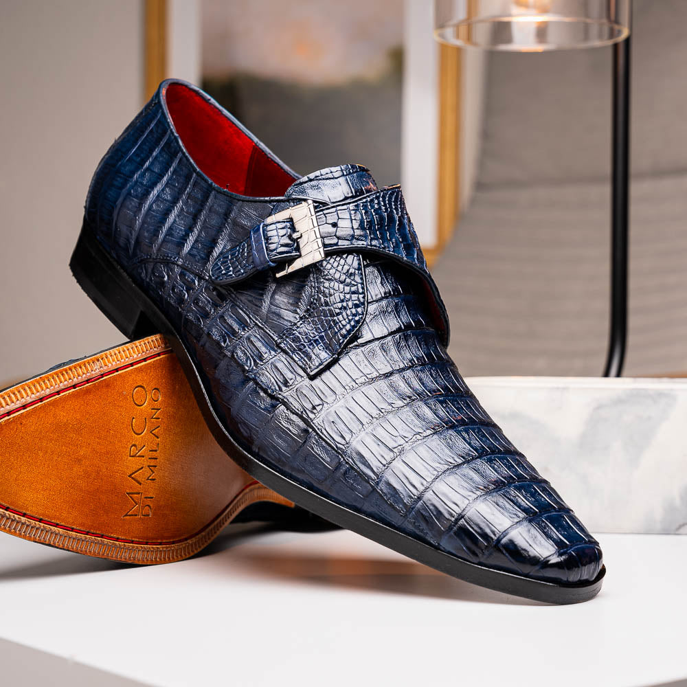 The Marco Di Milano Rovigo B Navy is a luxury men's monk strap shoe in blue crocodile-pattern leather, with one shoe upright and the other showing a tan sole stamped with the brand logo—perfect for dress shoe aficionados.