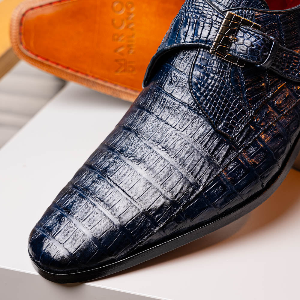 The Marco Di Milano Rovigo B Navy is a luxury men's monk strap shoe in blue crocodile-pattern leather, with one shoe upright and the other showing a tan sole stamped with the brand logo—perfect for dress shoe aficionados.