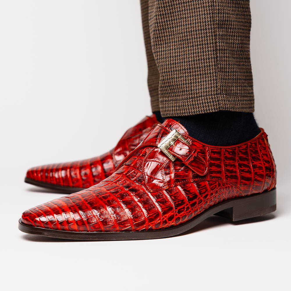 A pair of Rovigo Rustic Cognac monk strap dress shoes by Marco Di Milano, featuring shiny genuine caiman crocodile leather with a side buckle; one shoe is upright, and the other lies with its sole facing up.