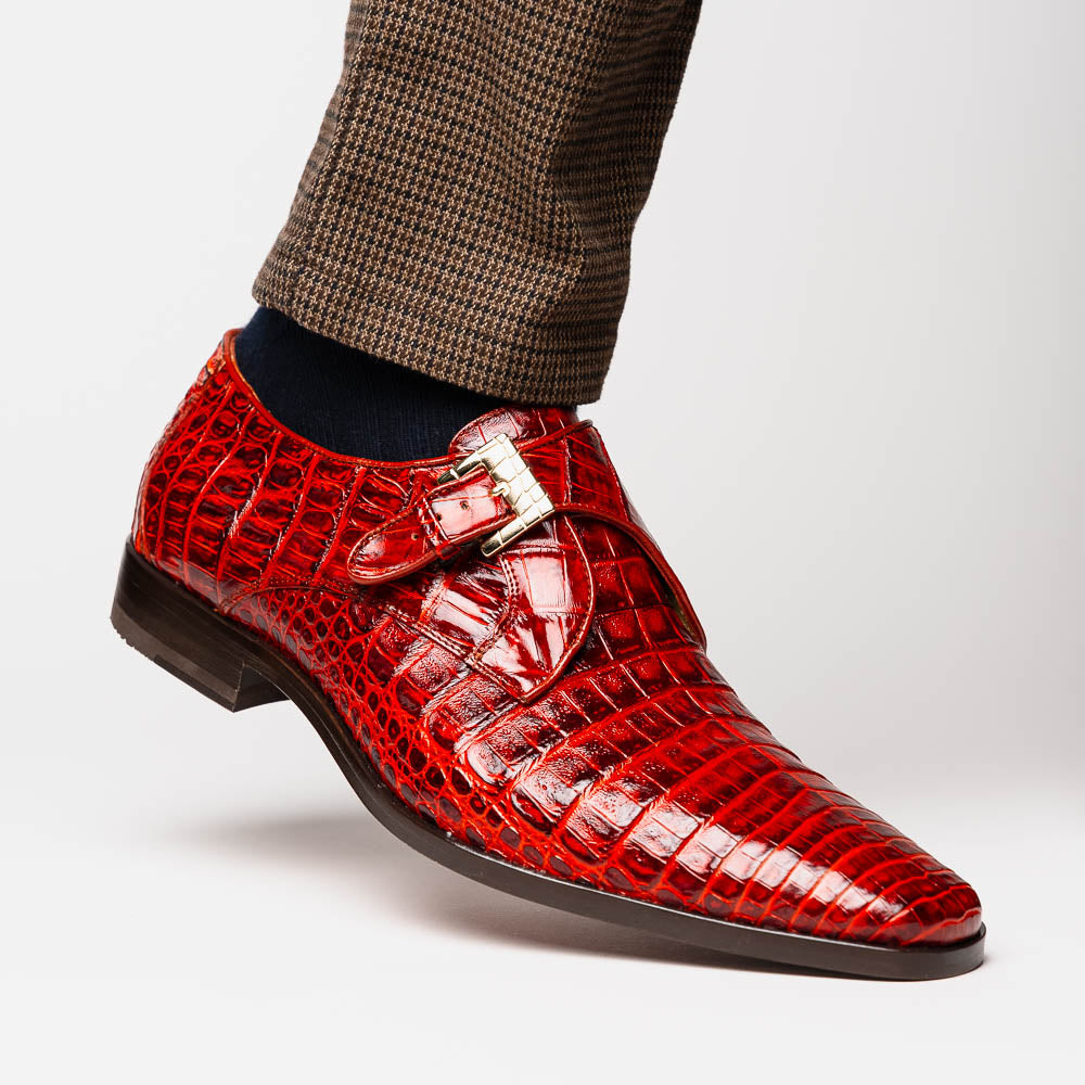 A pair of Rovigo Rustic Cognac monk strap dress shoes by Marco Di Milano, featuring shiny genuine caiman crocodile leather with a side buckle; one shoe is upright, and the other lies with its sole facing up.