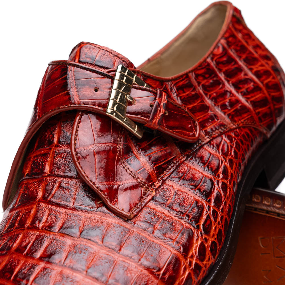 A pair of Rovigo Rustic Cognac monk strap dress shoes by Marco Di Milano, featuring shiny genuine caiman crocodile leather with a side buckle; one shoe is upright, and the other lies with its sole facing up.