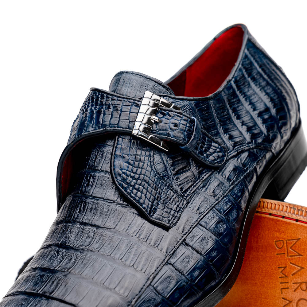 The Marco Di Milano Rovigo B Navy is a luxury men's monk strap shoe in blue crocodile-pattern leather, with one shoe upright and the other showing a tan sole stamped with the brand logo—perfect for dress shoe aficionados.