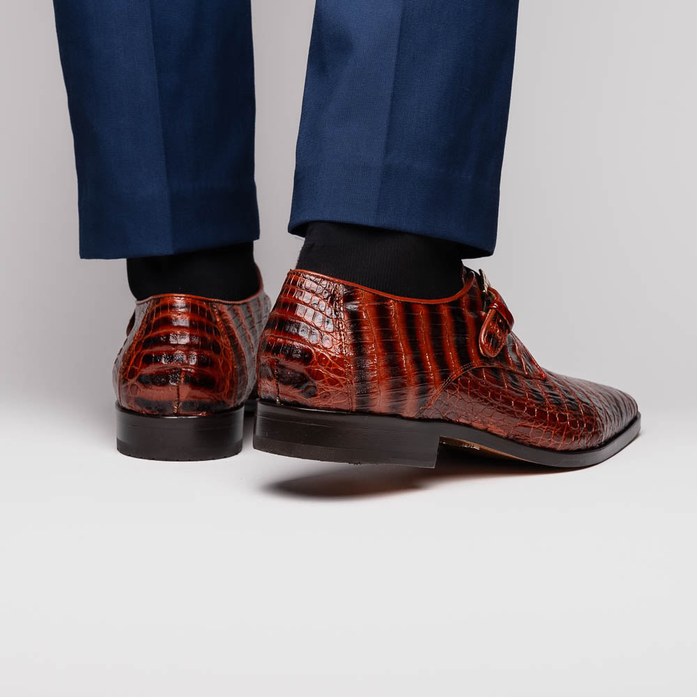 The Rovigo Cognac Straps by Marco Di Milano are brown genuine caiman crocodile monk strap dress shoes with a metal buckle—one upright, one on its side showing the branded sole. Luxury footwear for refined taste.