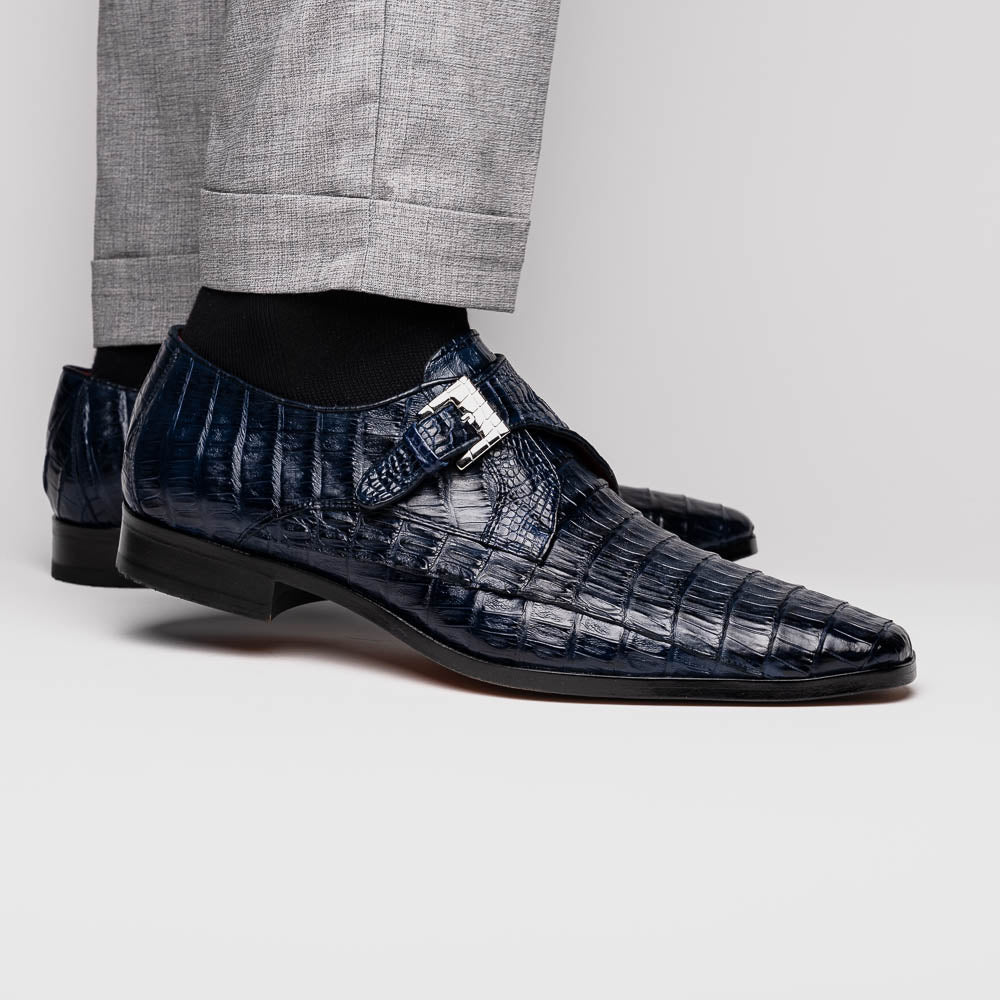 The Marco Di Milano Rovigo B Navy is a luxury men's monk strap shoe in blue crocodile-pattern leather, with one shoe upright and the other showing a tan sole stamped with the brand logo—perfect for dress shoe aficionados.