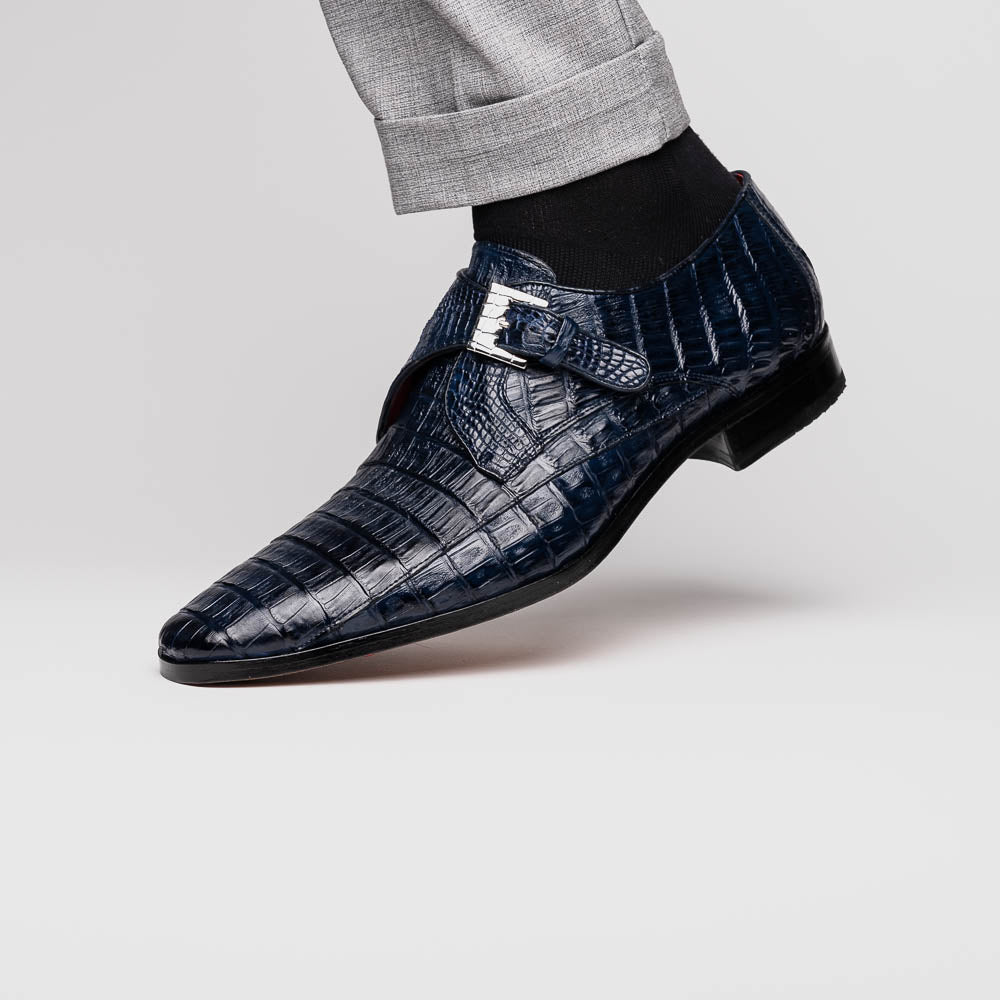 The Marco Di Milano Rovigo B Navy is a luxury men's monk strap shoe in blue crocodile-pattern leather, with one shoe upright and the other showing a tan sole stamped with the brand logo—perfect for dress shoe aficionados.