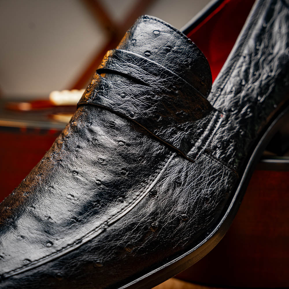 The Salvatore Black by Marco Di Milano is a pair of genuine ostrich leather loafers in black with a brown leather sole, detailed stitching, and an embossed brand logo on the outsole—ideal for luxury footwear enthusiasts.