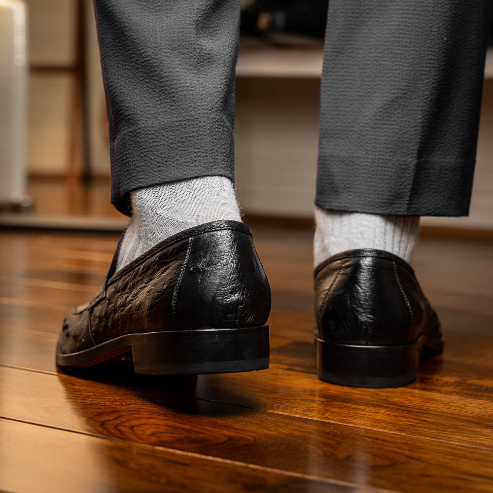 The Salvatore Black by Marco Di Milano is a pair of genuine ostrich leather loafers in black with a brown leather sole, detailed stitching, and an embossed brand logo on the outsole—ideal for luxury footwear enthusiasts.