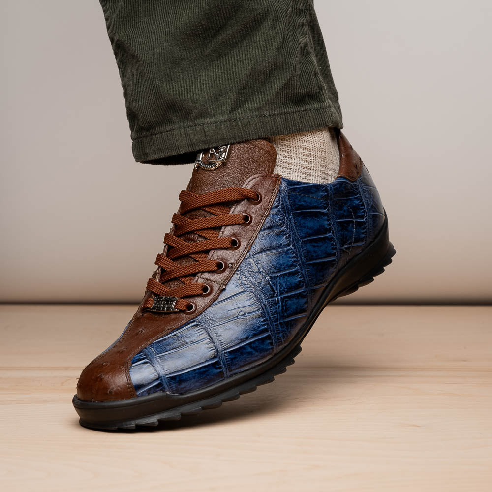 The Marco Di Milano Saulo Blue Jeans is a luxury men's sneaker featuring blue and brown hues, a textured crocodile-like pattern, and a black rubber sole, shown with one shoe upright and the other on its side.