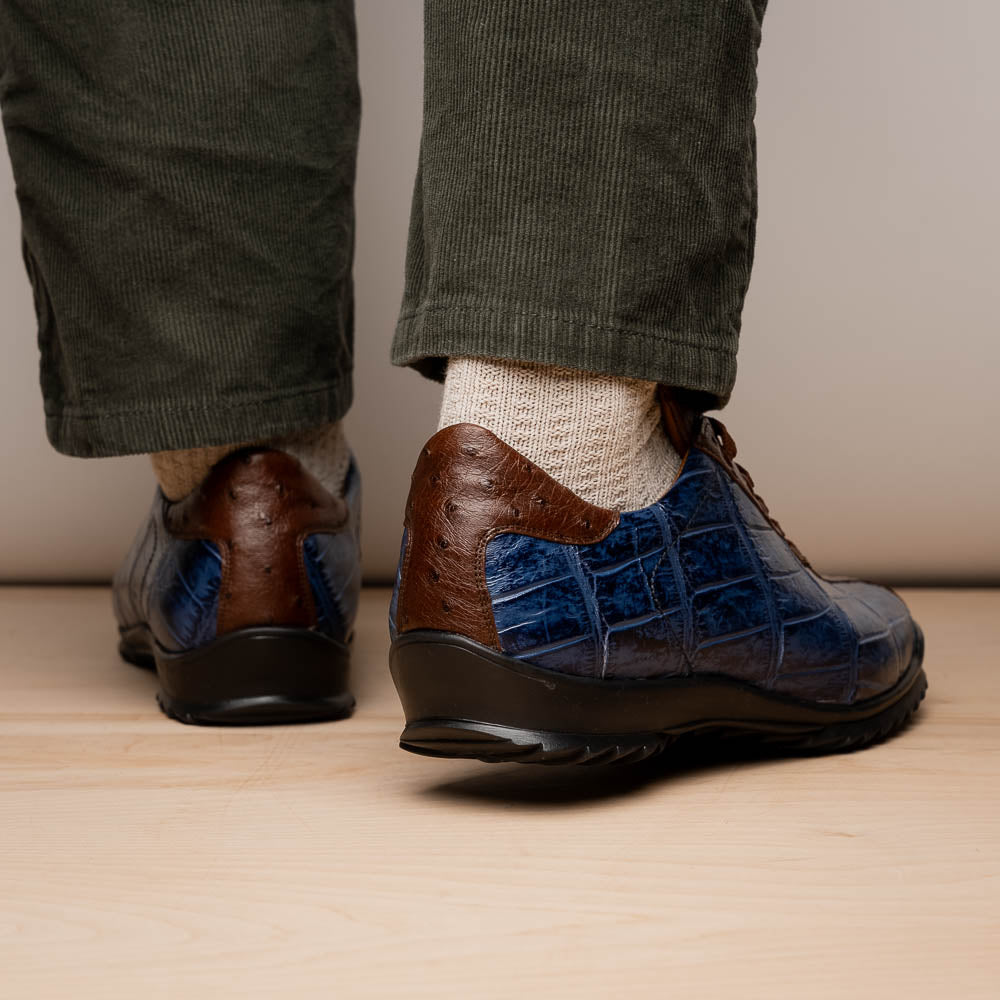 The Marco Di Milano Saulo Blue Jeans is a luxury men's sneaker featuring blue and brown hues, a textured crocodile-like pattern, and a black rubber sole, shown with one shoe upright and the other on its side.