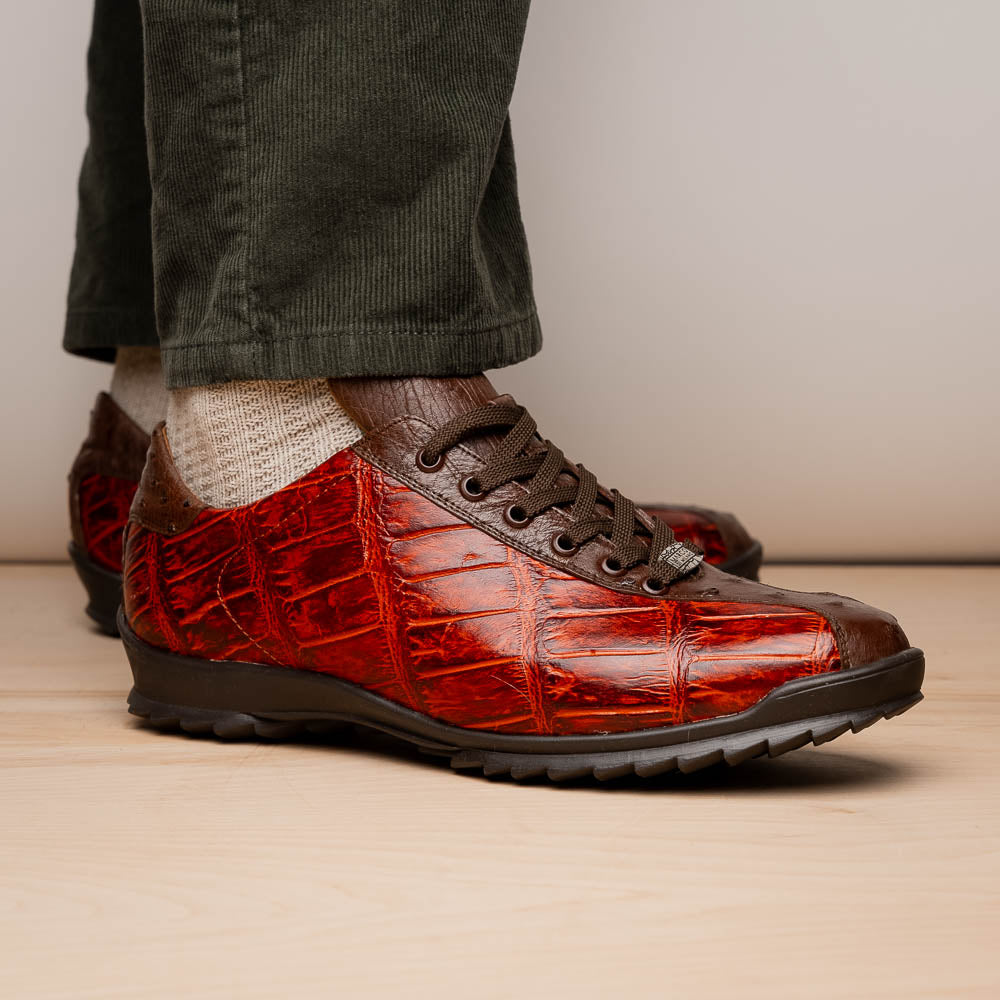 The Saulo Cognac sneakers by Marco Di Milano feature genuine alligator leather in red and brown with black laces and soles—an exceptional luxury men's footwear choice, shown with one upright and the other lying on its side.