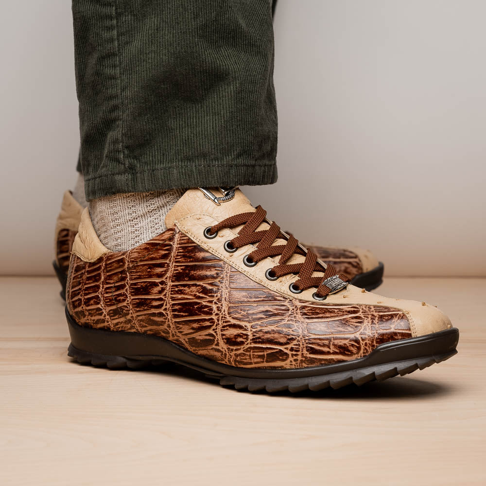 A pair of Saulo Orix men's shoes by Marco Di Milano, featuring brown crocodile-pattern leather and black rubber soles; one shoe stands upright while the other leans against it.