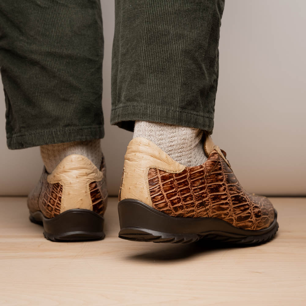 A pair of Saulo Orix men's shoes by Marco Di Milano, featuring brown crocodile-pattern leather and black rubber soles; one shoe stands upright while the other leans against it.