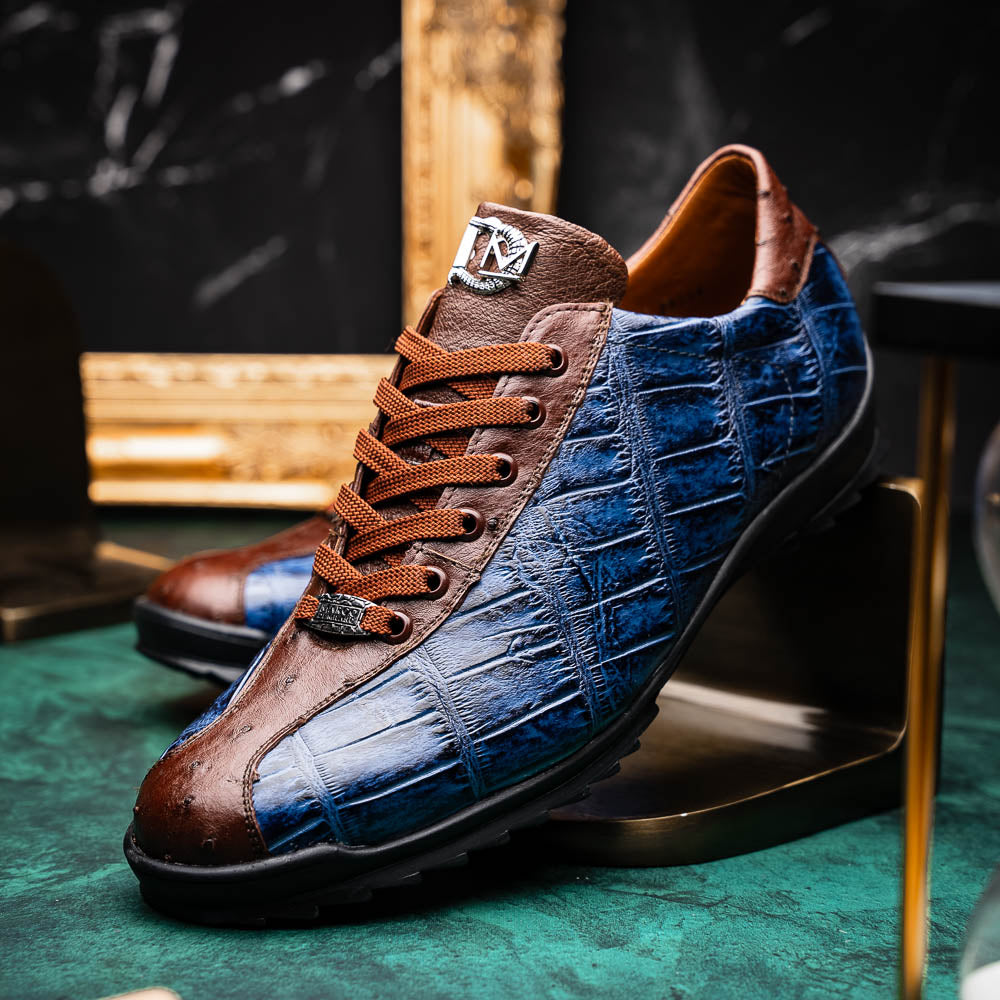 The Marco Di Milano Saulo Blue Jeans is a luxury men's sneaker featuring blue and brown hues, a textured crocodile-like pattern, and a black rubber sole, shown with one shoe upright and the other on its side.