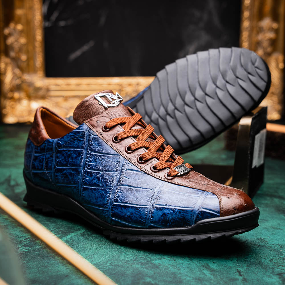 The Marco Di Milano Saulo Blue Jeans is a luxury men's sneaker featuring blue and brown hues, a textured crocodile-like pattern, and a black rubber sole, shown with one shoe upright and the other on its side.