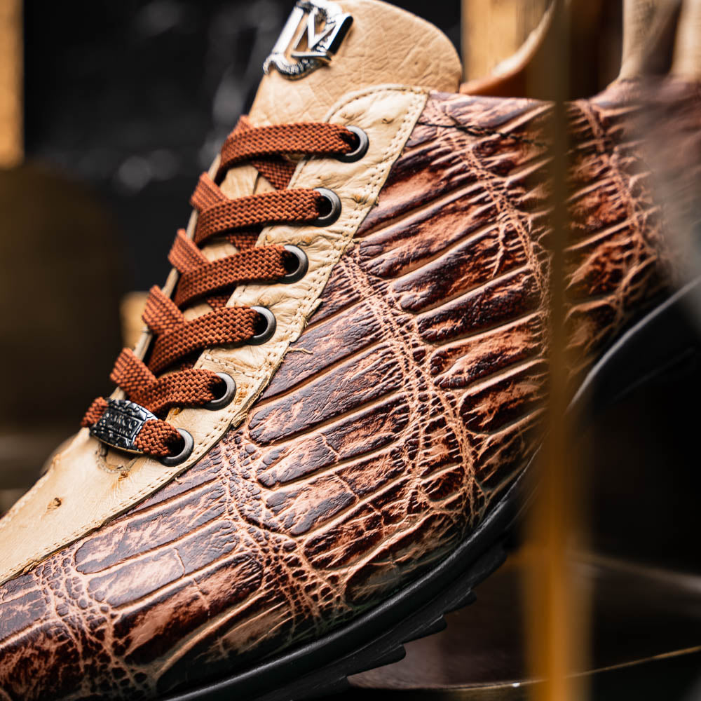 A pair of Saulo Orix men's shoes by Marco Di Milano, featuring brown crocodile-pattern leather and black rubber soles; one shoe stands upright while the other leans against it.