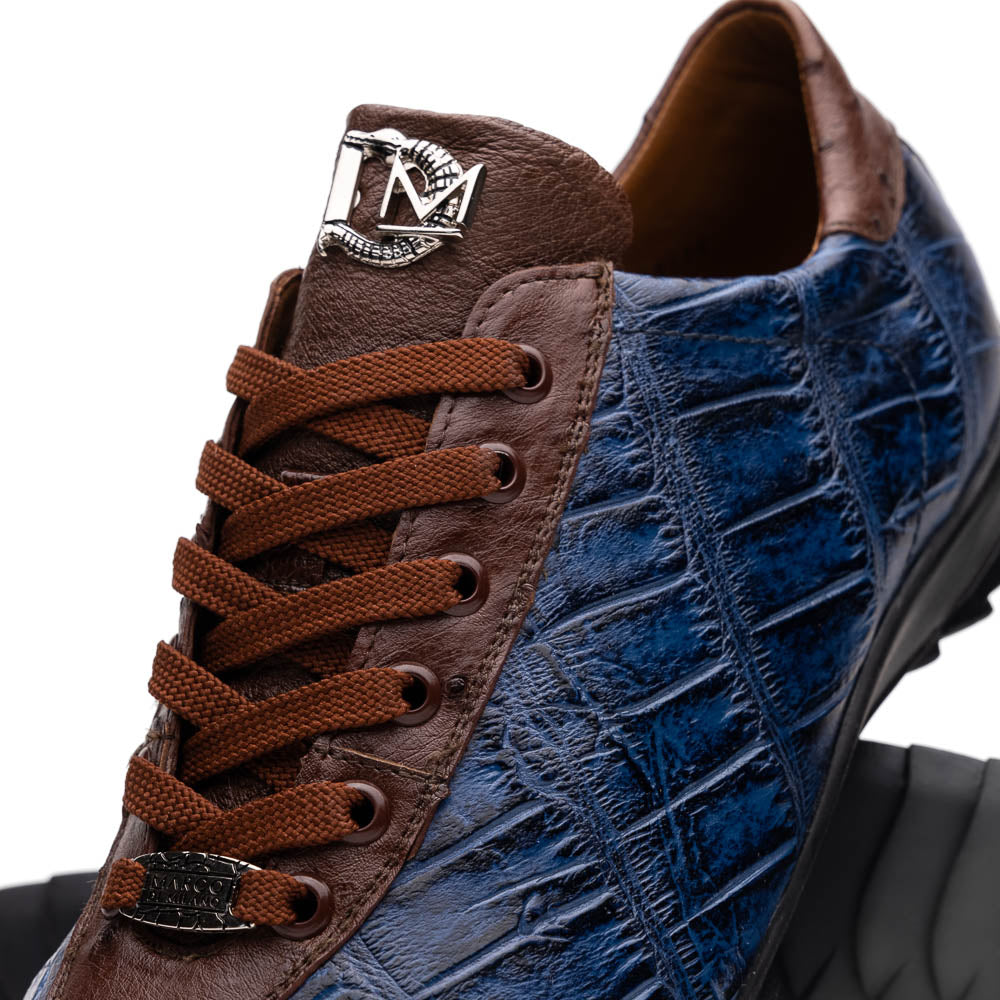 The Marco Di Milano Saulo Blue Jeans is a luxury men's sneaker featuring blue and brown hues, a textured crocodile-like pattern, and a black rubber sole, shown with one shoe upright and the other on its side.